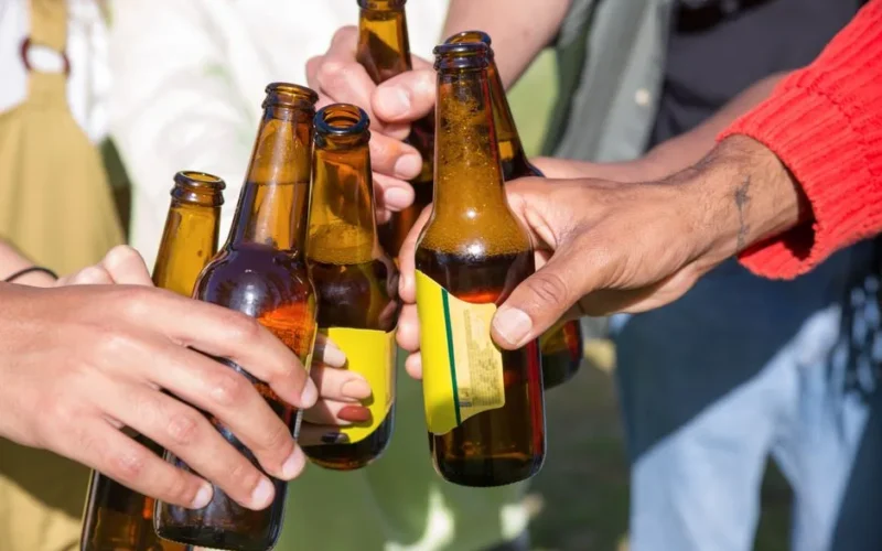 A group of people clinking beer bottles together in a celebratory toast outdoors.