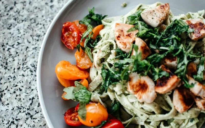 Savor a plate of chicken pesto pasta topped with fresh herbs and juicy cherry tomatoes.