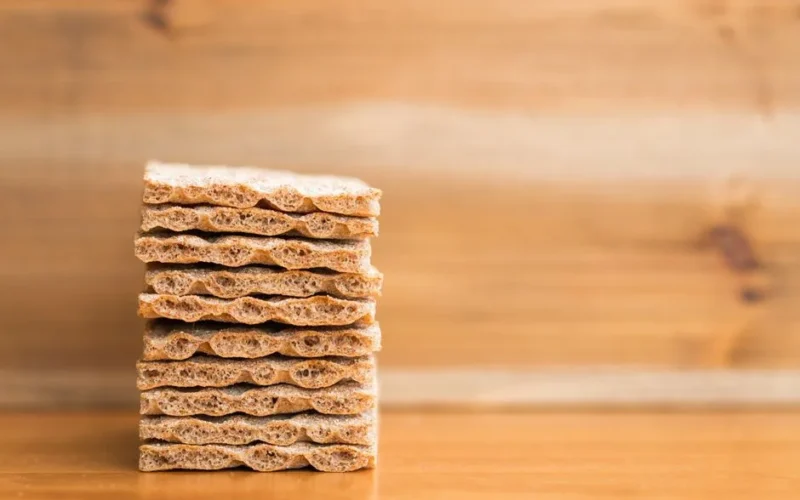 A neatly stacked pile of crispbread sits on a wooden surface with a blurred wooden backdrop.