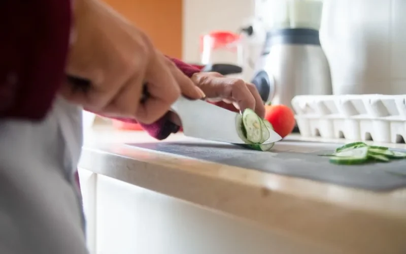 Close-up of a person slicing cucumbers on a kitchen counter for a healthy meal prep.