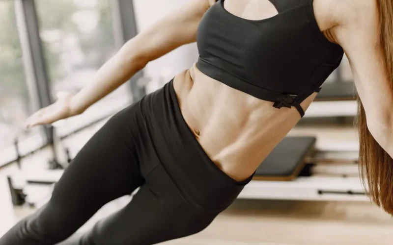 Fit woman in black sports outfit performing a side plank yoga pose on a mat indoors.