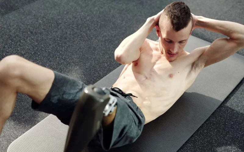 A determined man with a prosthetic leg doing sit-ups on a yoga mat indoors, showcasing strength and resilience.
