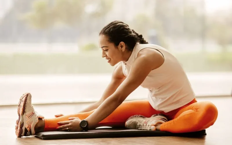 A woman performing a hamstring stretch indoors, promoting fitness and flexibility.
