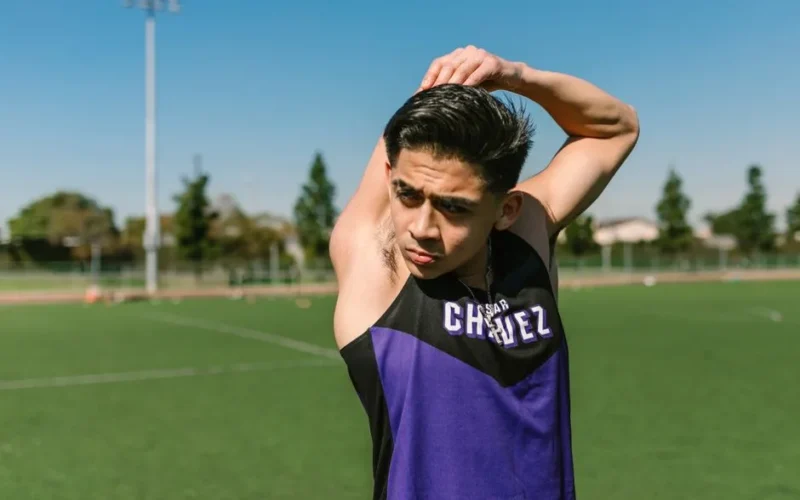 A young male athlete stretches on a sunny soccer field, preparing for practice.