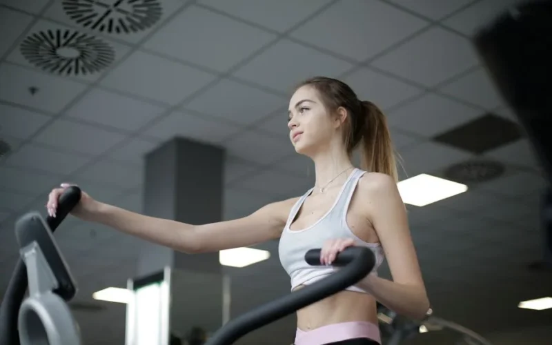 Focused woman working out on elliptical trainer, showcasing fitness and determination indoors.