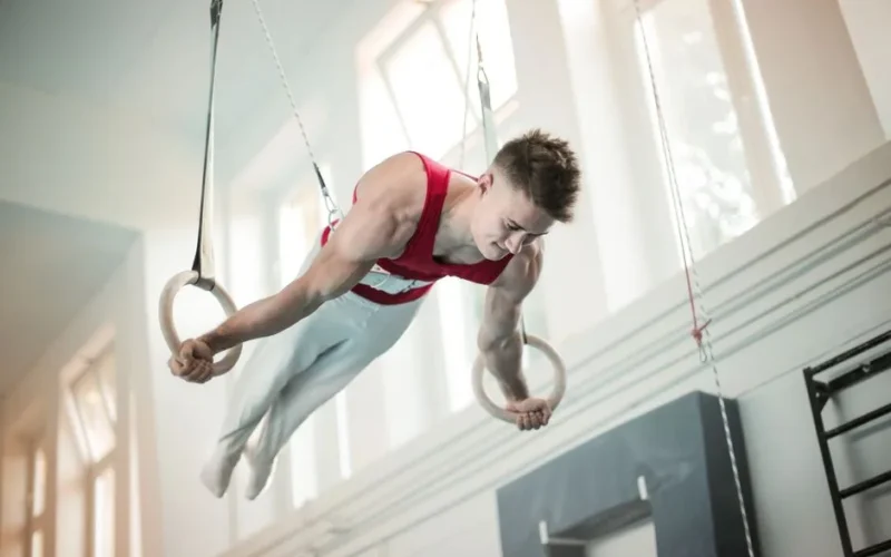 A male gymnast showcases strength and balance on rings during practice inside a gym.