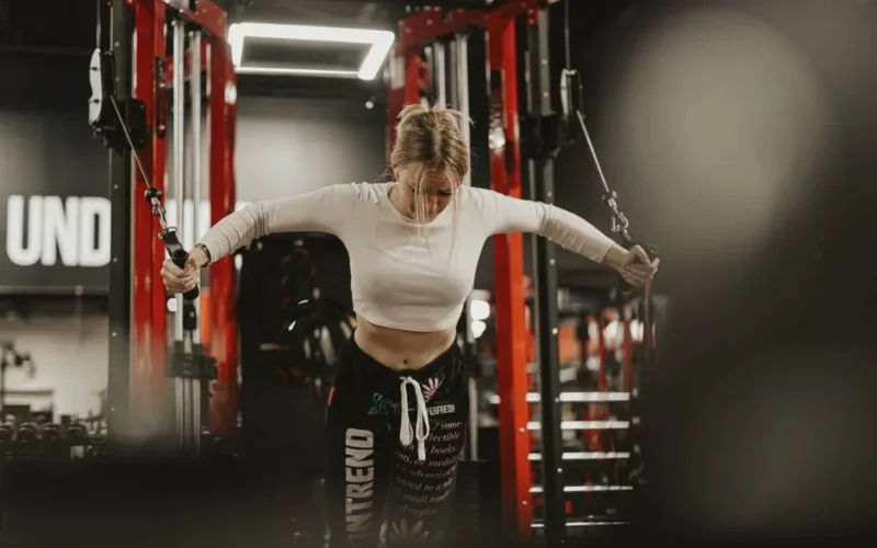 Focused young woman working out using a cable machine in a modern gym environment.