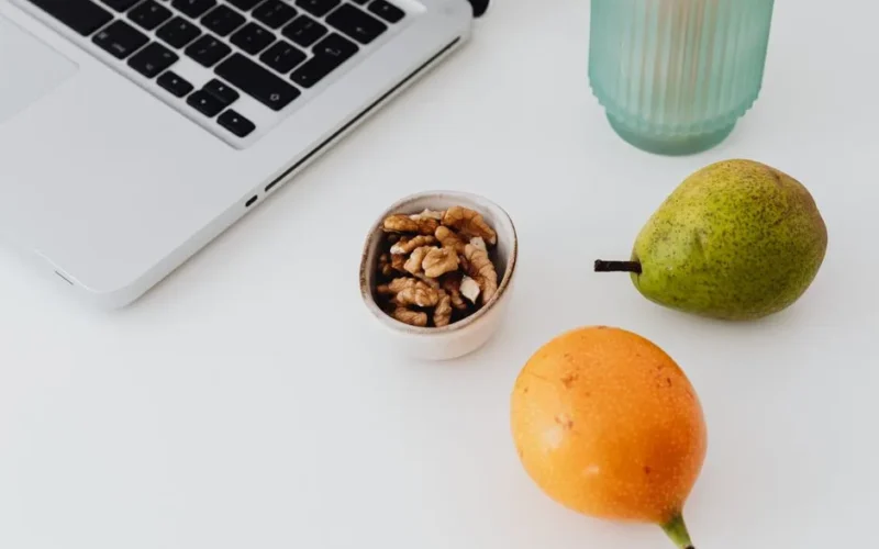 A desk setup featuring a laptop, fruits, and snacks for a productive and healthy work environment.
