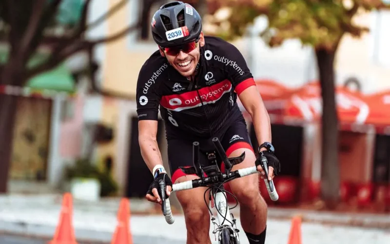 Smiling cyclist in helmet racing on road bike during a sunny day.