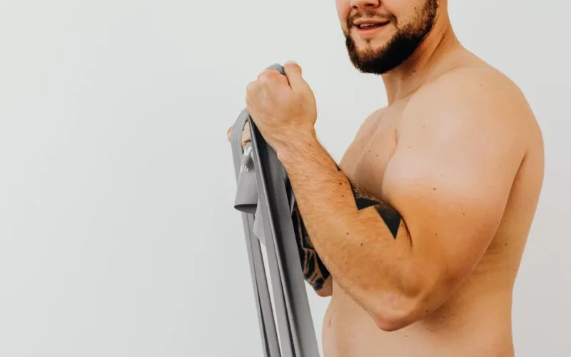 Shirtless man using resistance band for strength training indoors.