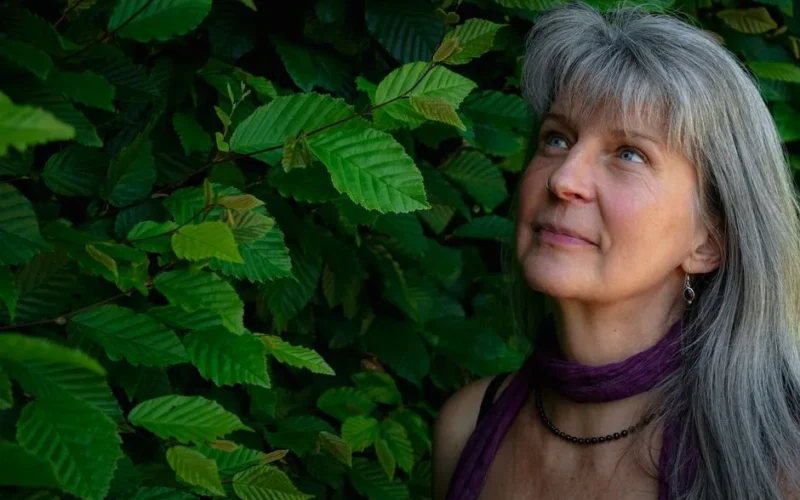 A serene moment of a mature woman surrounded by lush green leaves in Königshain.