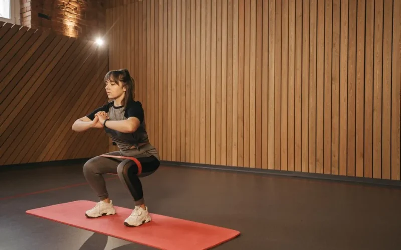 Young woman exercises indoors with resistance band on mat for fitness