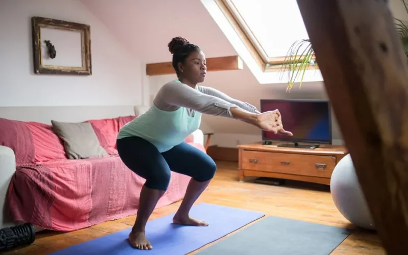 A woman performs squats on a yoga mat in a cozy living room, promoting home fitness and wellness.