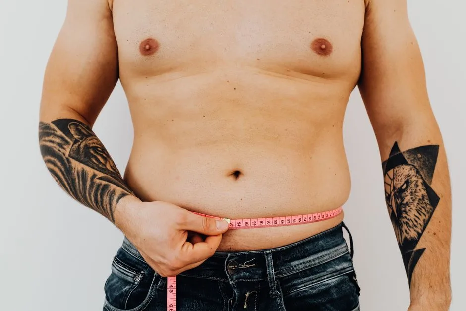 A man with tattoos measures his waist with a tape, focusing on fitness or weight loss.