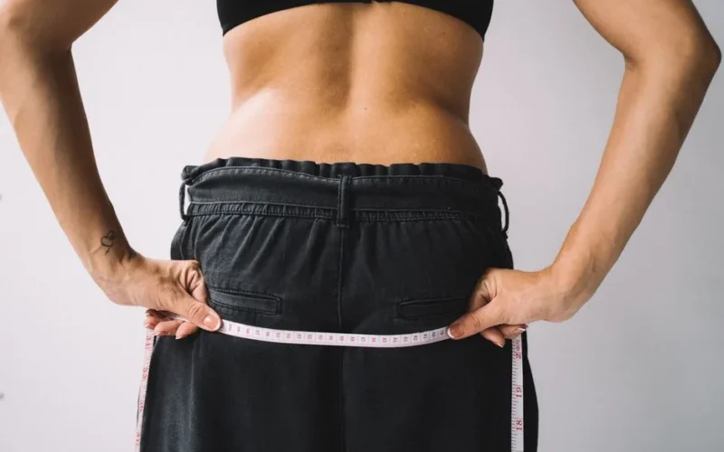 A person measuring their waist with a tape measure, symbolizing fitness goals.