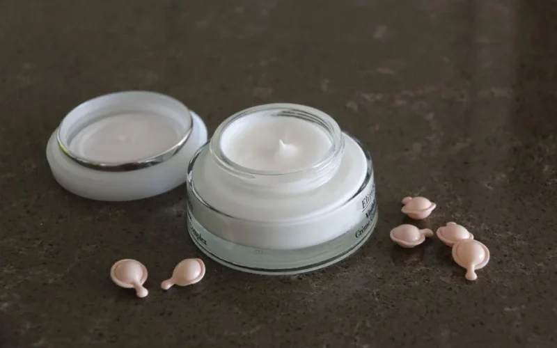 Open jar of luxurious face cream with capsules on a dark textured surface for skincare routines.