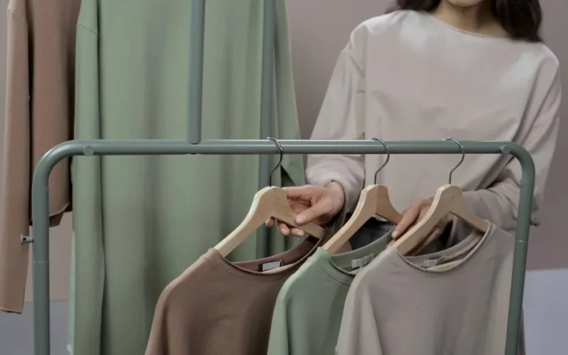 Woman choosing neutral colored sweaters from a clothing rack in a modern store.