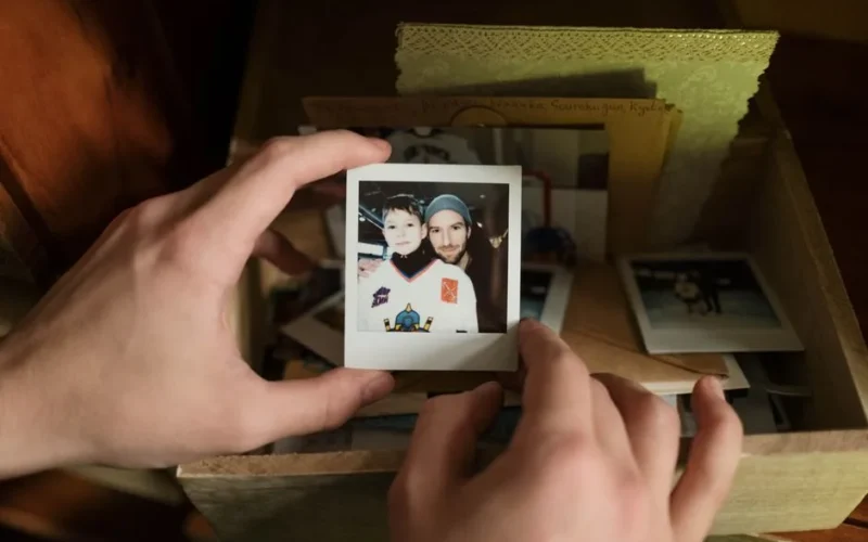 Close-up of hands holding a nostalgic Polaroid photo of father and son from a memory box.