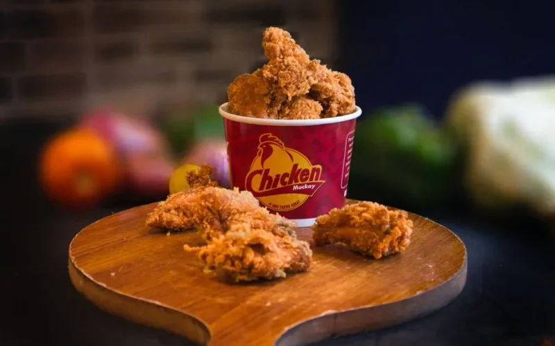 Mouth-watering fried chicken in a bucket displayed beautifully with blurred vegetables in the background.