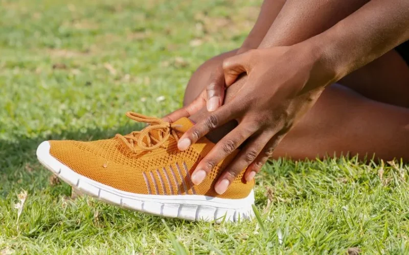 Person holding ankle in orange sneaker, suggesting potential sports injury.