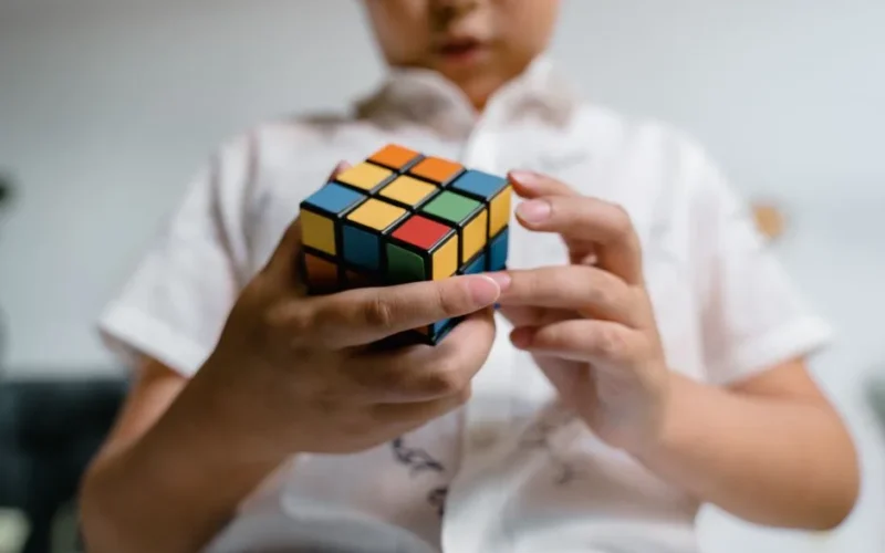 Focused child solving a Rubik's Cube indoors, highlighting intellect and problem-solving.