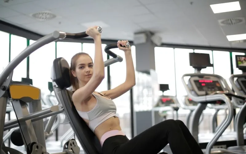 A young woman works out on a gym machine inside a modern fitness center, focusing on strength and health.