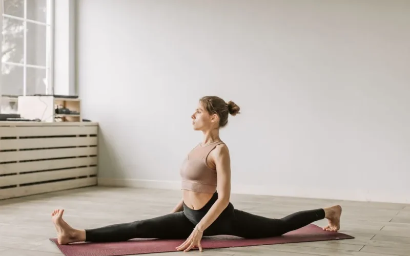 Adult woman stretching on a yoga mat indoors, demonstrating flexibility and focus.