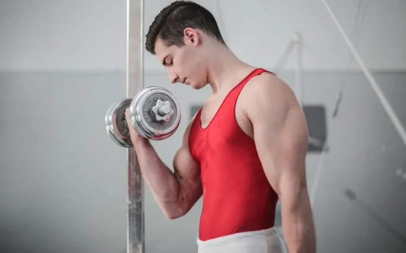 Muscular man in red outfit performing a dumbbell curl for strength training indoors.