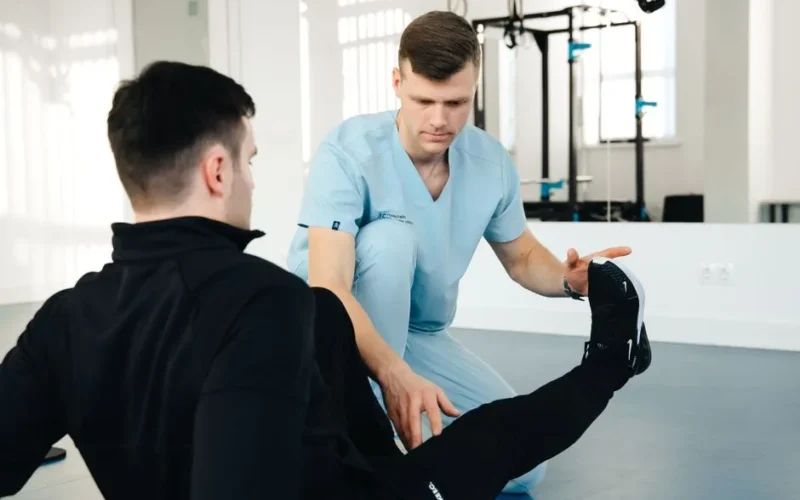 A physiotherapist assisting a patient in leg exercises during a rehabilitation session in a clinic setting.