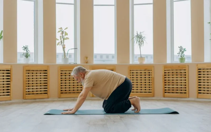 Elderly man kneeling on a yoga mat in a serene indoor setting for mindfulness and health.