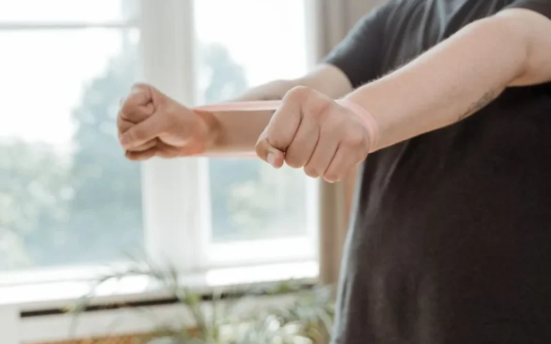 A man uses a resistance band for arm exercises in a bright indoor setting.