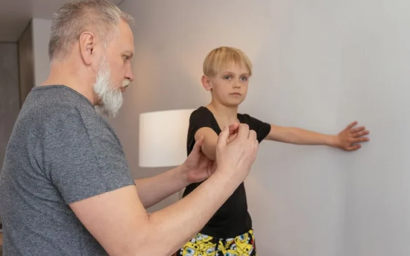 A grandfather guiding his grandson in physical exercise at home for a healthy lifestyle.