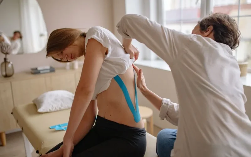 Chiropractor uses kinesio tape for pain relief on woman's back in a therapy session.
