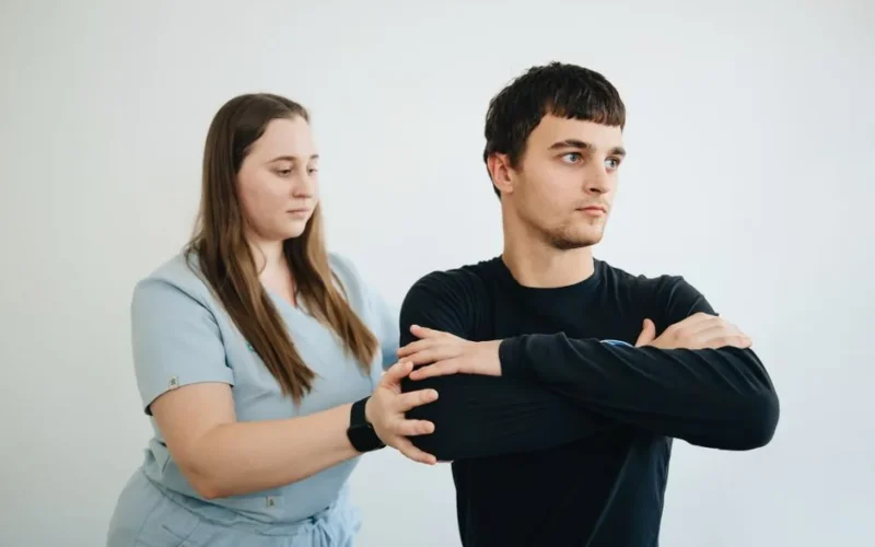 A physiotherapist assists a patient with arm exercises in a clinical setting.