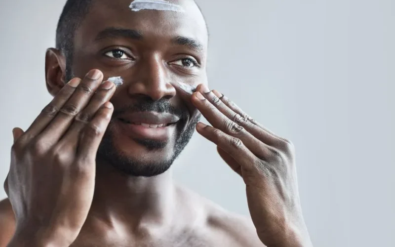 Smiling man applying face cream as part of his daily skincare routine for healthy skin.