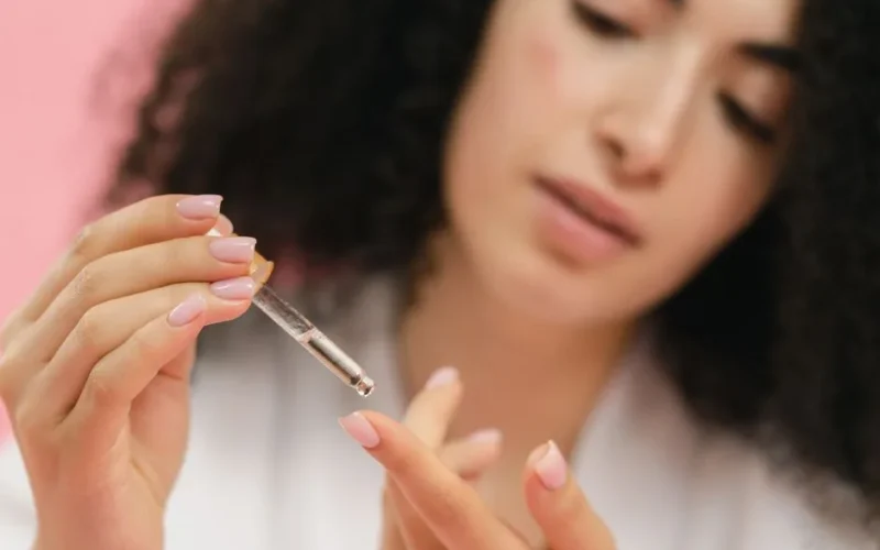 Close-up of a young woman applying skincare serum with a pipette against a pink background.
