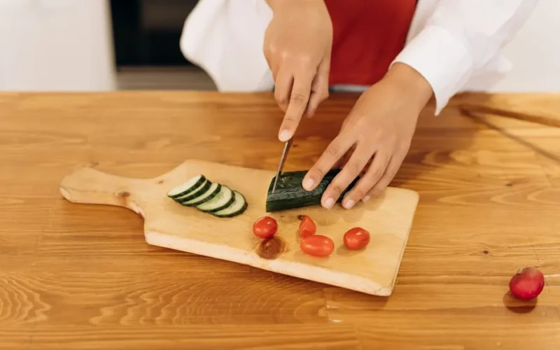 A woman slices cucumbers and cherry tomatoes for a healthy salad in a modern kitchen.