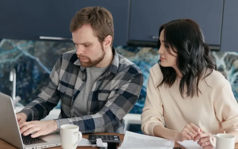A couple working together on financial planning at home, using a laptop and paperwork.