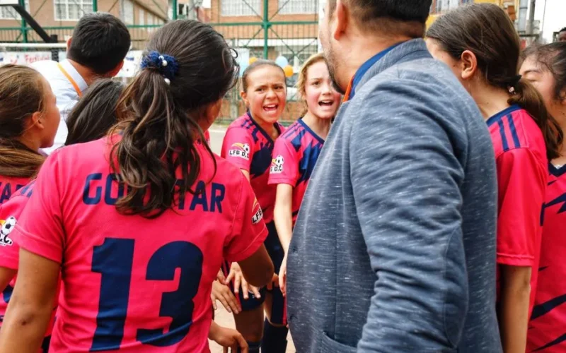 A vibrant moment capturing a youth soccer team in a motivational huddle with their coach, outdoors.