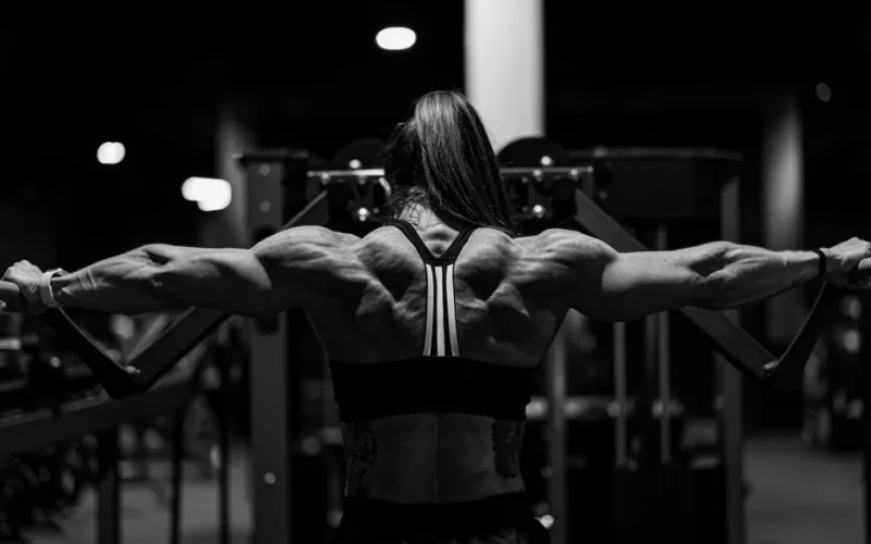 Black and white photo of a strong woman exercising in a gym with focus on back muscles.