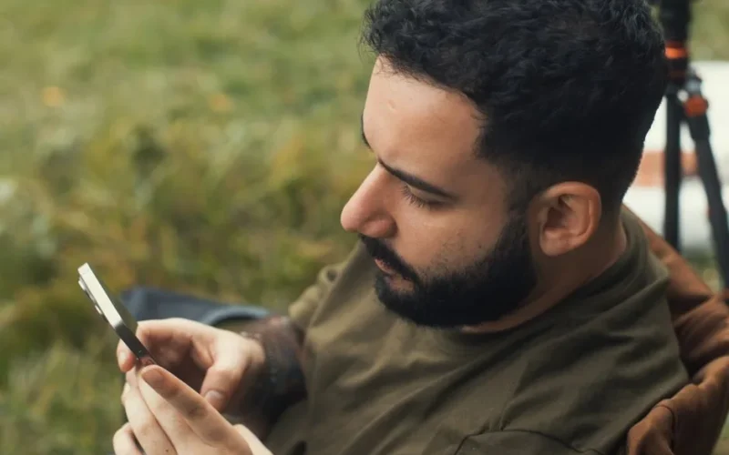 Young man using smartphone while relaxing outdoors, showcasing modern connectivity.