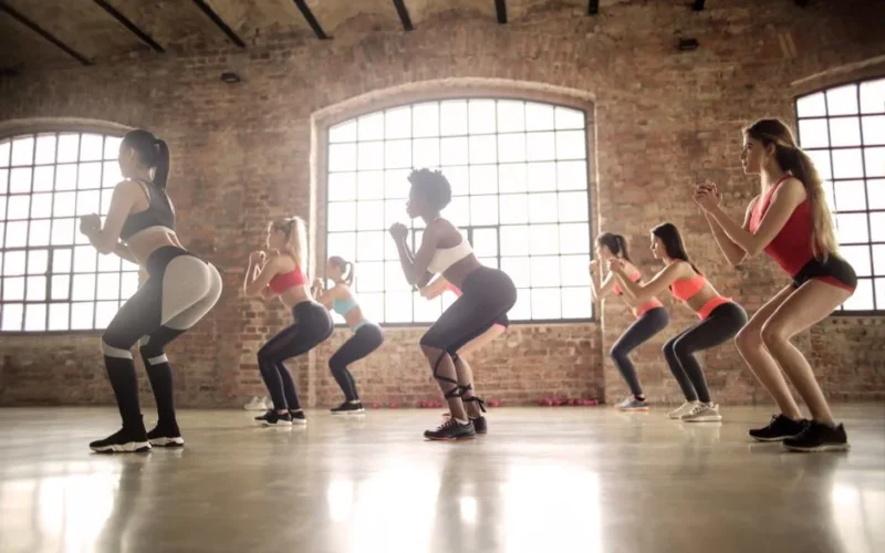 Women participating in a group fitness class performing squats in an industrial-style studio.