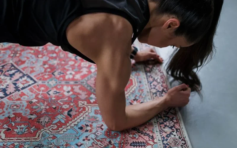 Woman performing a plank exercise on a patterned rug, showcasing muscular strength and focus.
