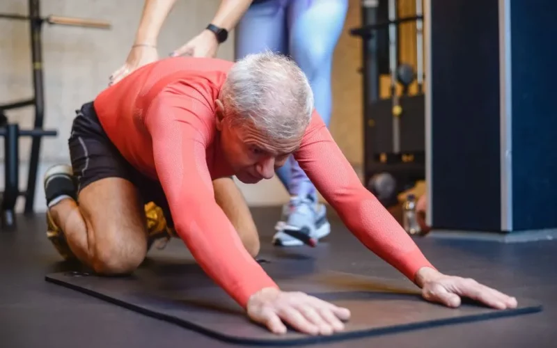 Senior man engaging in assisted stretching exercises for healthy living in a gym.