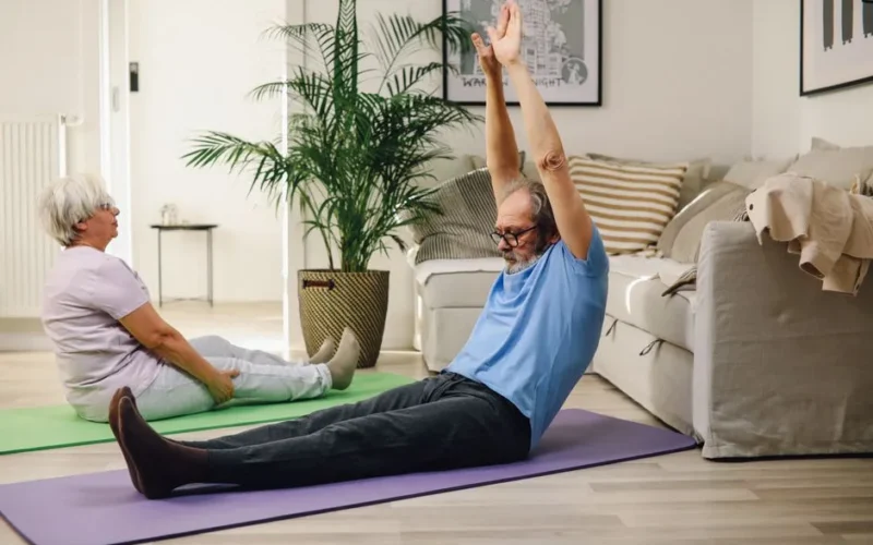 Elderly couple enjoying yoga exercise on mats at home, promoting healthy and positive aging.