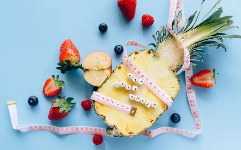 A sliced pineapple with berries and a tape measure on a blue background promoting healthy eating.