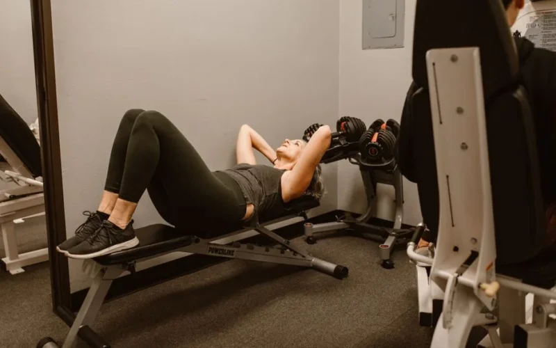 Adult woman exercising on a bench in a gym, promoting fitness and healthy lifestyle.