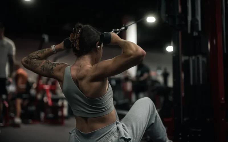 Woman performs strength training with a cable machine in a modern gym setting.