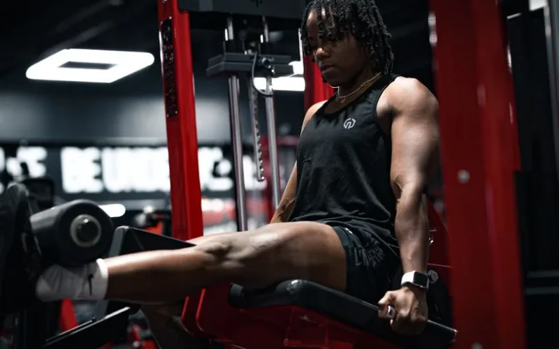 Muscular individual focusing on leg exercises in a gym setting, emphasizing strength and fitness.