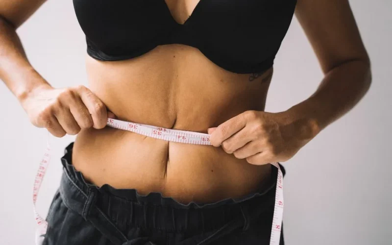 A woman measures her waist with a tape for fitness and weight loss results.